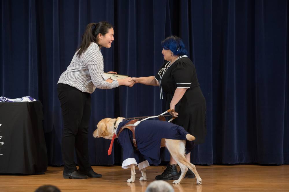 GSA President shaking hands with a professor receiving an award. The professor's service dog is onstage